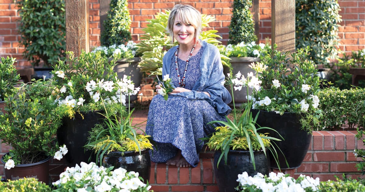 Linda Vater in a blue print dress sits on a brick pathway among Southern Living plants