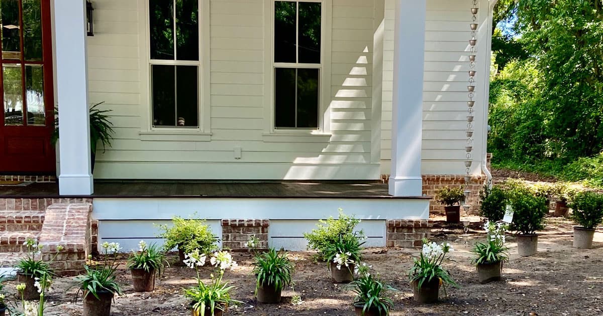 White slat house with low porch and new arrangement of Southern Living 1 gallon plants placed for planting