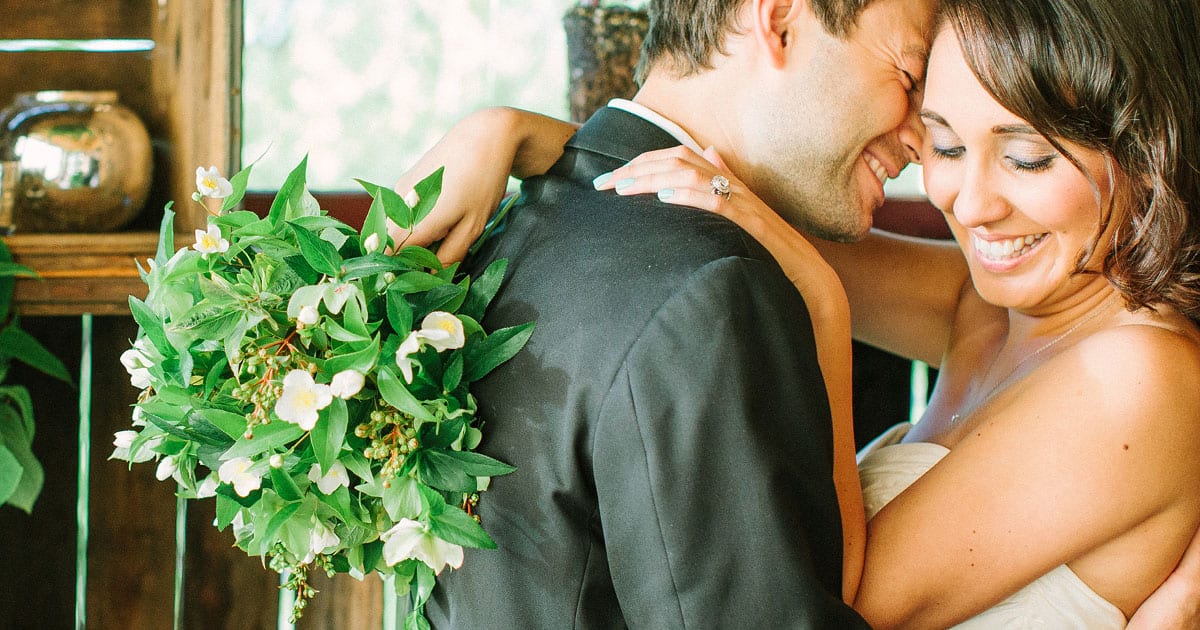 Groom's back with Bride's arms draped around his back holding a bouquet made of Empress of China Dogwood