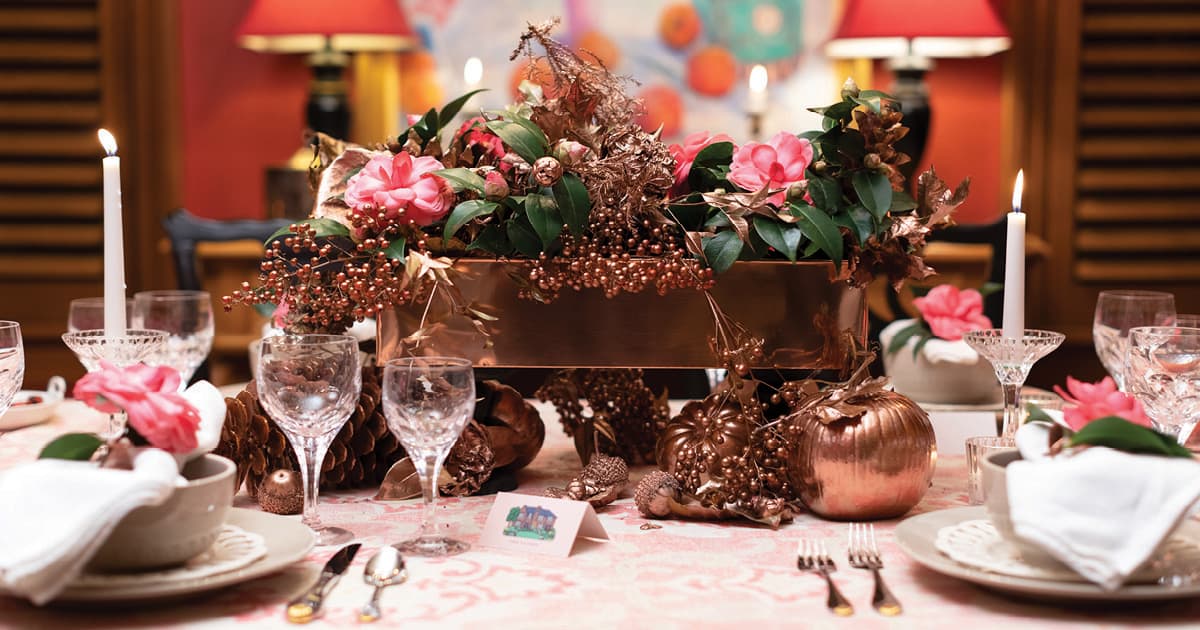 Thanksgiving copper container holding pink roses with cream dinnerware and white lit candles