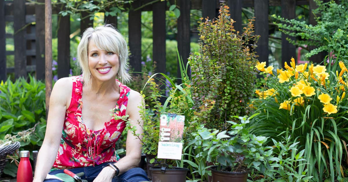 Linda Vater in a red blouse posing with newly arrived Southern Living plants before she plants them in her garden